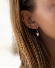 A close-up lifestyle shot of a woman wearing a small gold hoop earring with a dangling heart-shaped crystal charm.